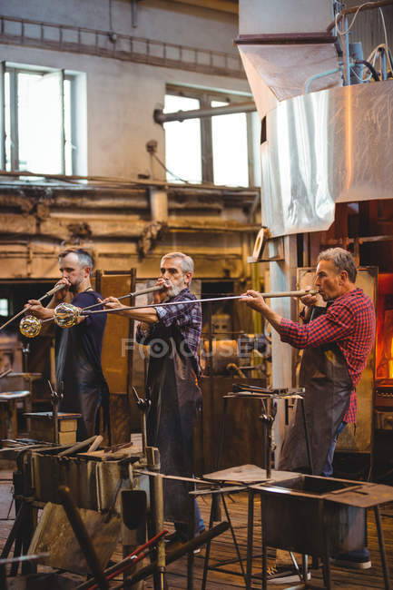 Team of glassblowers shaping a glass on the blowpipes at glassblowing factory — Stock Photo