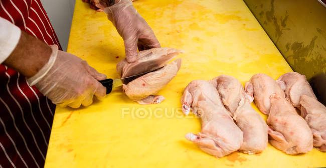Manos de carnicero picando pollo en el mostrador de trabajo en la carnicería - foto de stock