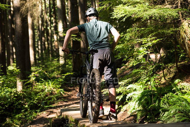 Vue arrière du cycliste masculin marchant en VTT en forêt — Photo de stock