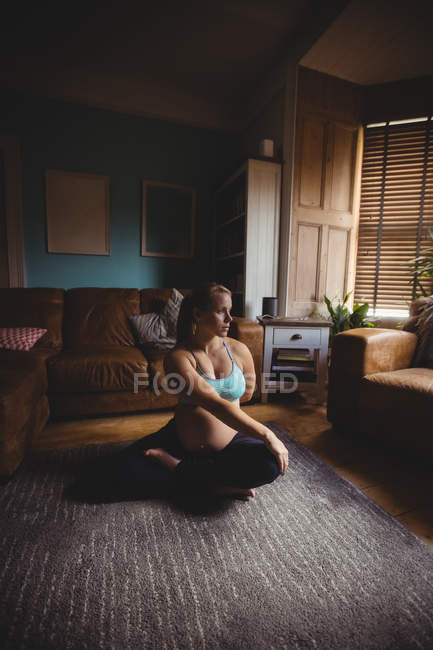 Deportivo Mujer embarazada realizando ejercicio de estiramiento en la sala de estar en casa - foto de stock