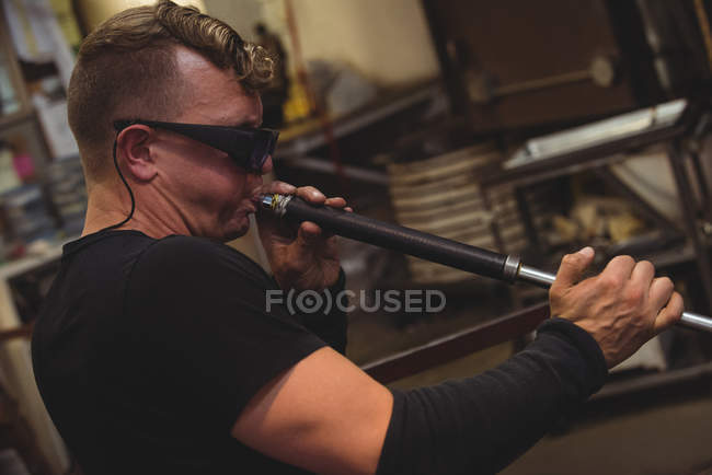 Glassblower shaping piece of glass on blowpipe at glassblowing factory — Stock Photo