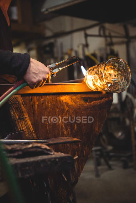 Стеклодув дает заключительный штрих куску стекла со стеклодувной горелкой на стекольном заводе — стоковое фото