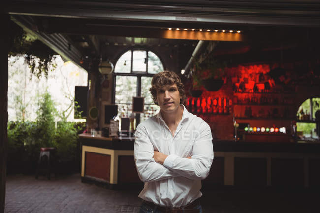 Portrait of smiling man standing with arms crossed in bar — Stock Photo