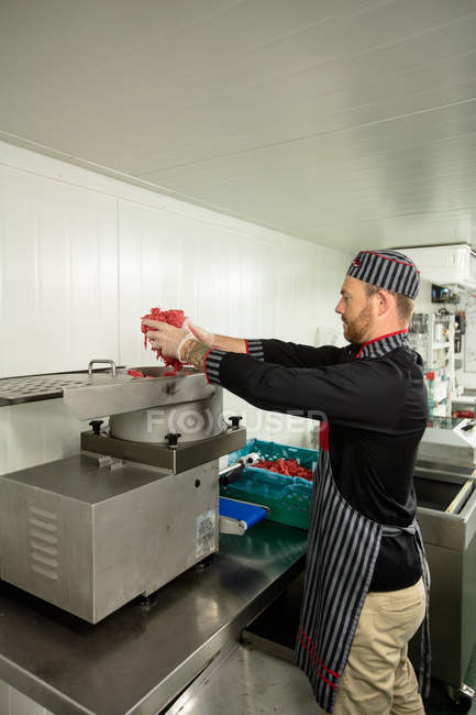 Butcher putting meat in mincer machine at butchers shop — Stock Photo