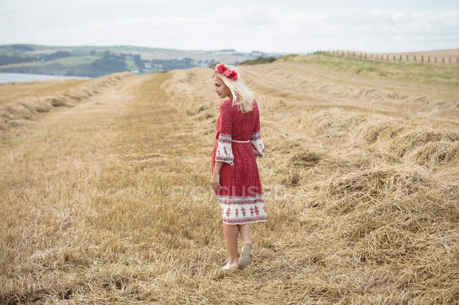 Rear view of carefree blonde woman in red dress walking in field — Stock Photo