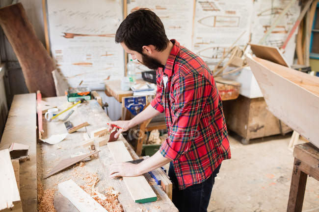 Hombre trabajando sobre una tabla de madera en el astillero - foto de stock