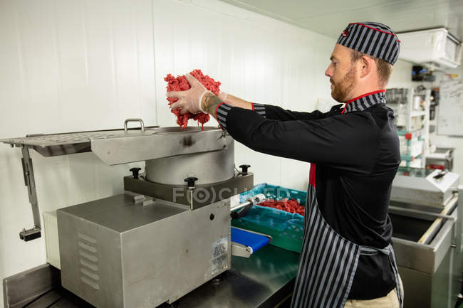 Butcher putting meat in mincer machine at butchers shop — Stock Photo