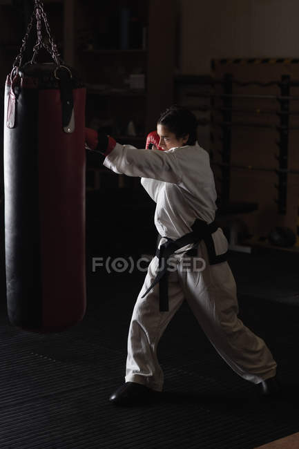 Vue latérale de la femme pratiquant le karaté avec sac de boxe dans le studio de fitness — Photo de stock