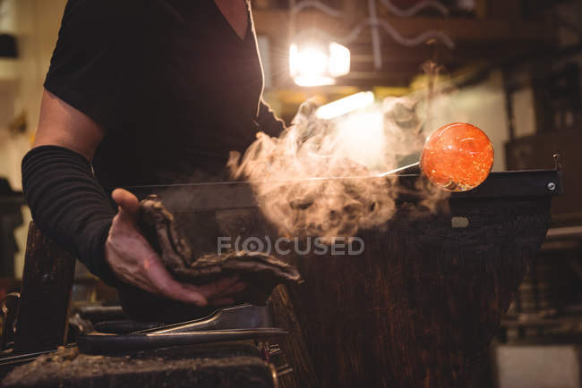 Geschnittenes Bild des Glasbläsers, der in der Glasbläserei mit feuchtem Tuch geschmolzenes Glasstück formt — Stockfoto