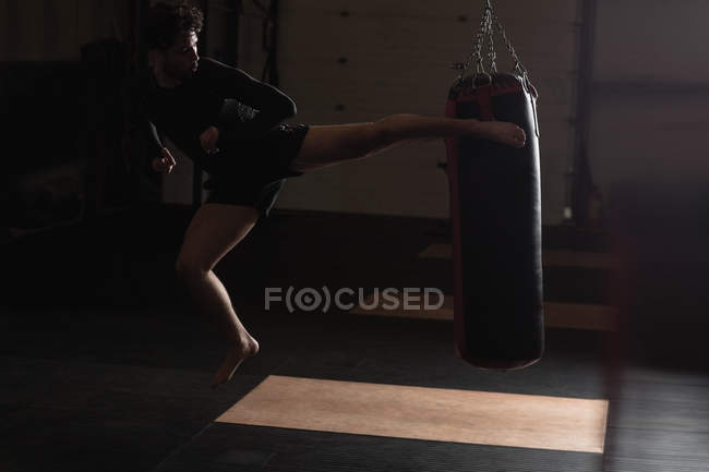 Боксер занимается боксом с боксерской грушей в темной фитнес-студии — стоковое фото