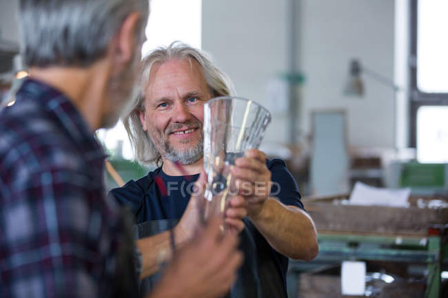 Стеклодувка показывает стеклянную вазу коллеге на стеклодувном заводе — стоковое фото