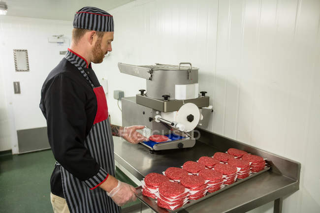Carnicero preparando hamburguesas crudas en la carnicería - foto de stock
