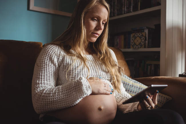 Femme enceinte utilisant une tablette numérique dans le salon à la maison — Photo de stock