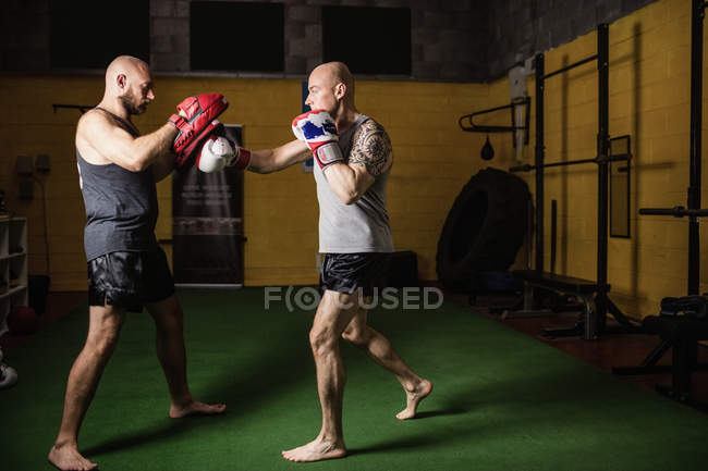Vue latérale de deux boxeurs thaï sportifs pratiquant dans la salle de gym — Photo de stock
