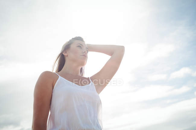 Vista de ángulo bajo de la mujer con la mano en el pelo de pie en el campo de trigo en el día soleado - foto de stock