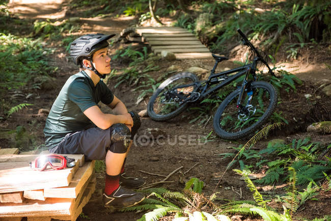 Продуманий чоловічий велосипедист сидить у лісі в сонячний день — стокове фото