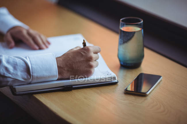 Рука бизнесмена, пишущего в дневнике за столом в офисе — стоковое фото