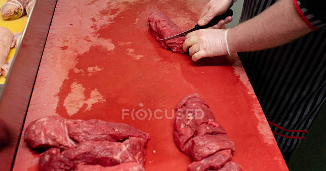 Hands of butcher chopping red meat at butchers shop — Stock Photo