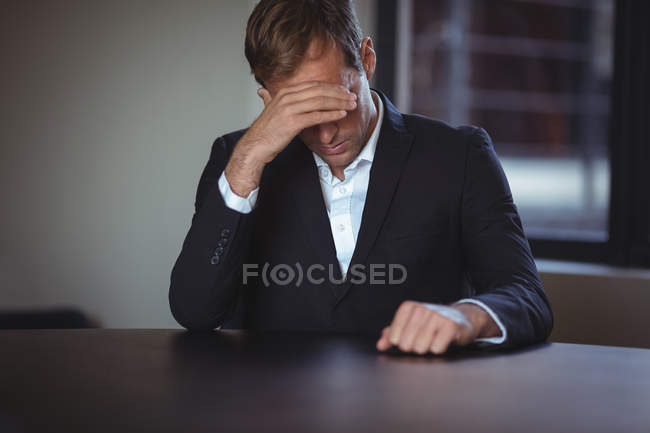 Напряженный бизнесмен сидит в офисе с рукой на висках — стоковое фото