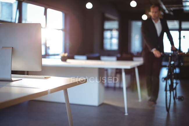 Businessman standing with a bicycle in office — Stock Photo