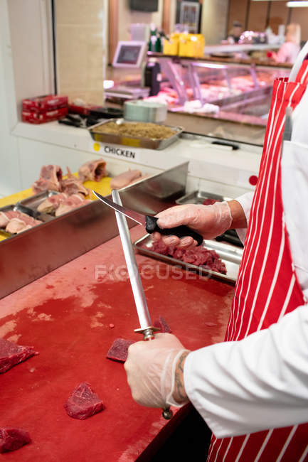 Mid section of butcher sharpening knife in butchers shop — Stock Photo