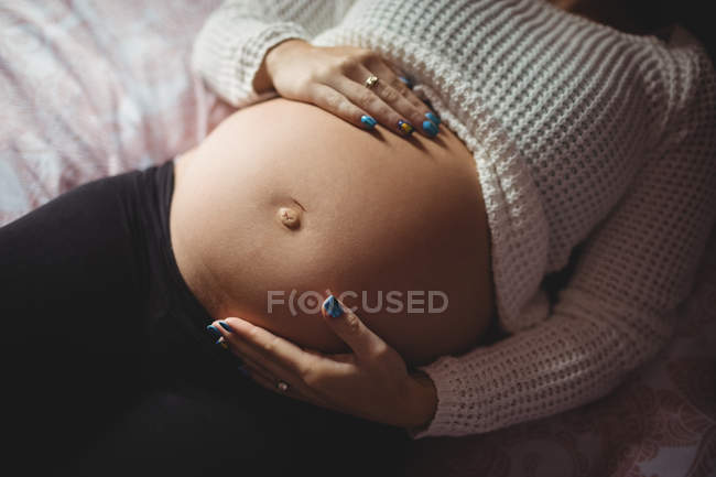 Sección media de la mujer embarazada que se relaja en el dormitorio en casa - foto de stock