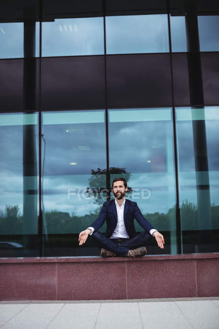 Businessman practicing yoga outside office building — Stock Photo