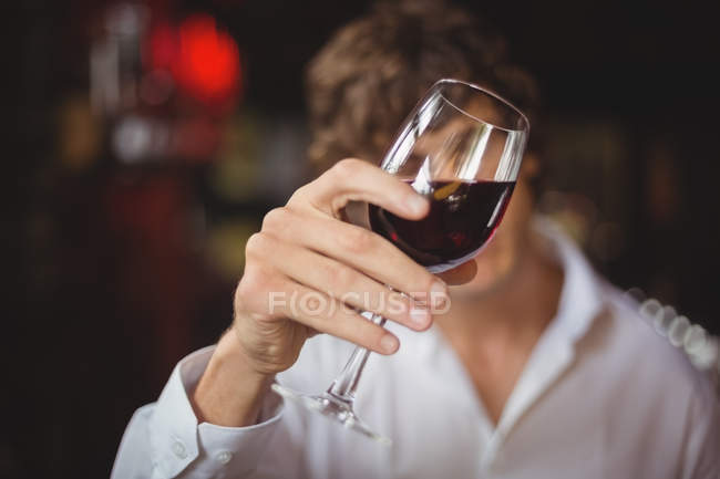 Camarero mirando una copa de vino tinto en el mostrador del bar - foto de stock