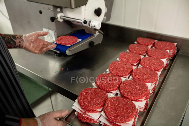 Mid section of butcher preparing a raw hamburger patties in butchers shop — Stock Photo