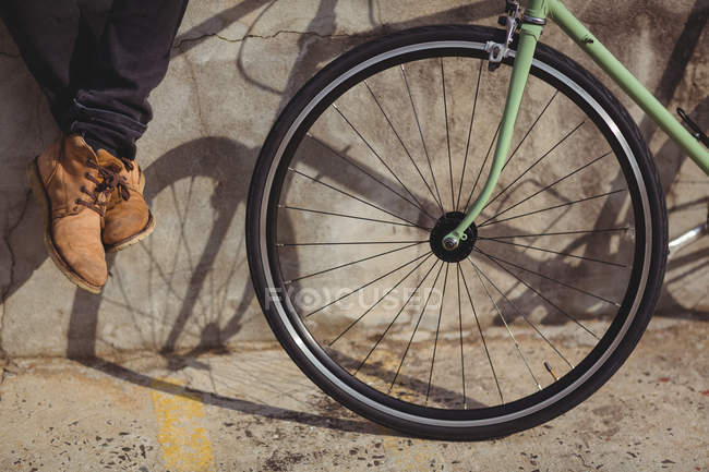 Обрезанное изображение человека, сидящего на стене рядом с велосипедом — стоковое фото