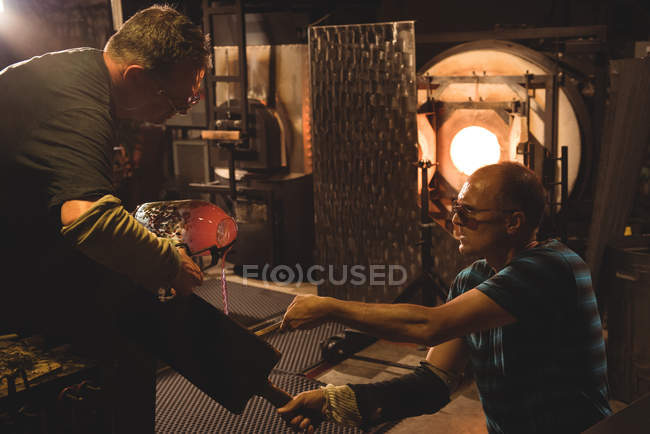 Команда стеклодувов, формирующих расплавленное стекло на стекольном заводе — стоковое фото