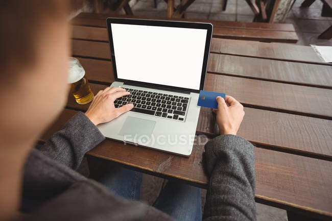 Man doing online shopping with credit card on laptop in bar — Stock Photo