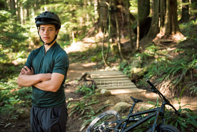 Портрет велосипедиста мужского пола, стоящего со скрещенными в лесу руками — стоковое фото