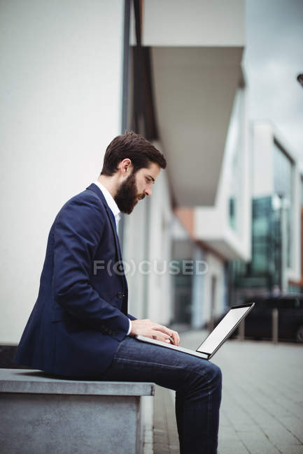 Hombre de negocios atento utilizando el ordenador portátil fuera de la oficina - foto de stock