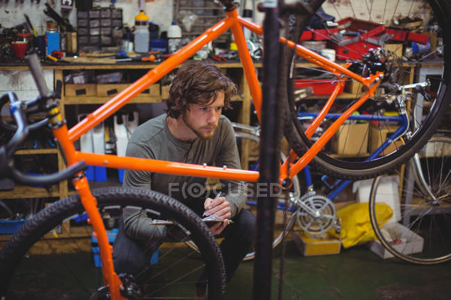 Mechanic writing on clipboard in bicycle shop — Stock Photo