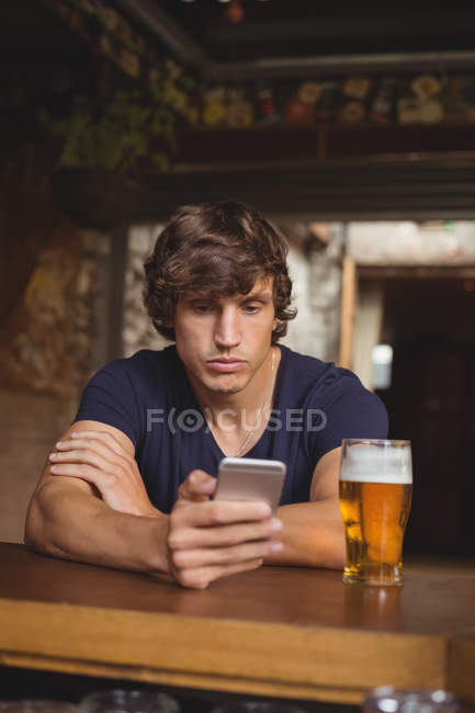 Homem usando telefone celular com copo de cerveja na mesa no bar — Fotografia de Stock