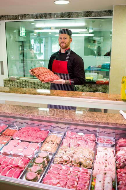 Carnicero parado en el mostrador de carne en la carnicería - foto de stock