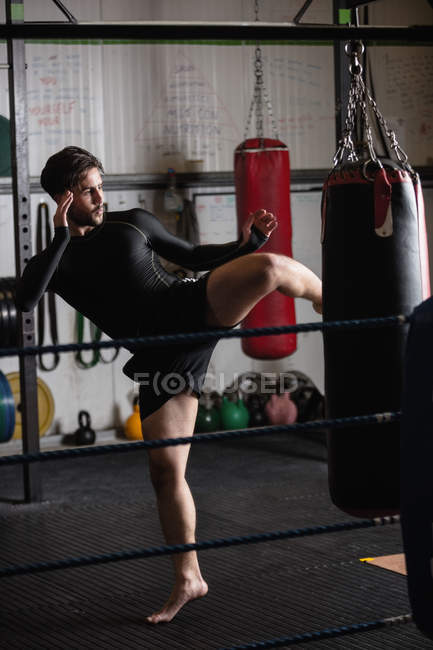Vista lateral del boxeador practicando boxeo con saco de boxeo en gimnasio - foto de stock