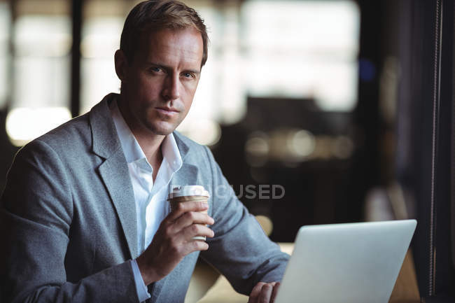 Retrato del hombre de negocios trabajando en el ordenador portátil mientras toma café en la cafetería - foto de stock