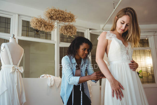 Mujer probándose el vestido de novia en un estudio con la ayuda del diseñador de moda - foto de stock