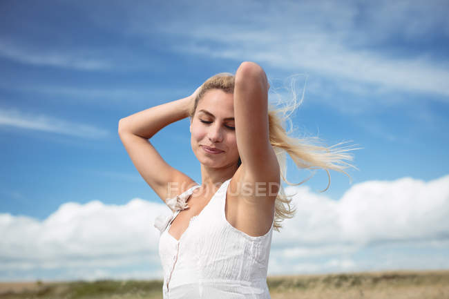 Привабливим блондинки жінку, що стояли в полі руками в волосся — стокове фото