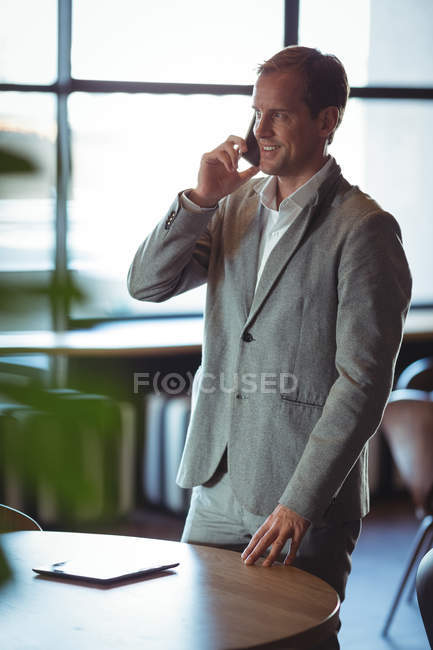 Un hombre de negocios sonriente hablando por teléfono móvil en un café - foto de stock