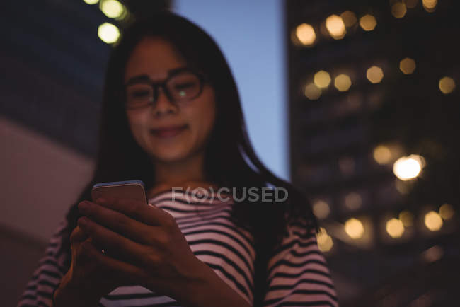 Jeune femme utilisant le téléphone portable dans la ville la nuit — Photo de stock
