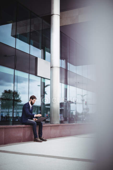 Businessman sitting in passage of office building and using laptop — Stock Photo