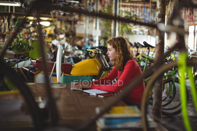 Жінка сидить за столом і використовує комп'ютер у велосипедному магазині — стокове фото