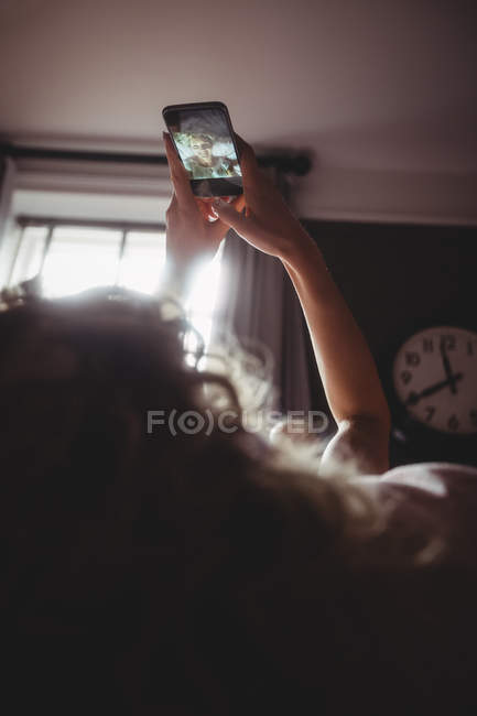 Femme prenant selfie sur téléphone portable dans la chambre à coucher à la maison — Photo de stock