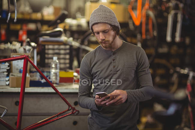 Mechanic using mobile phone in bicycle shop — Stock Photo