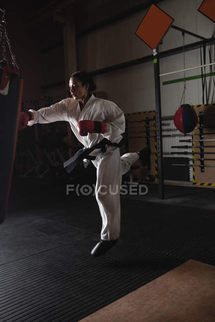 Femme pratiquant le karaté avec sac de boxe dans un studio de fitness sombre — Photo de stock