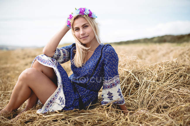 Despreocupado mujer rubia en vestido azul sentado en el campo y mirando a la cámara - foto de stock