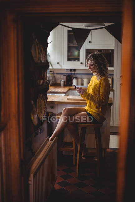 Belle femme utilisant un téléphone portable dans la cuisine à la maison — Photo de stock